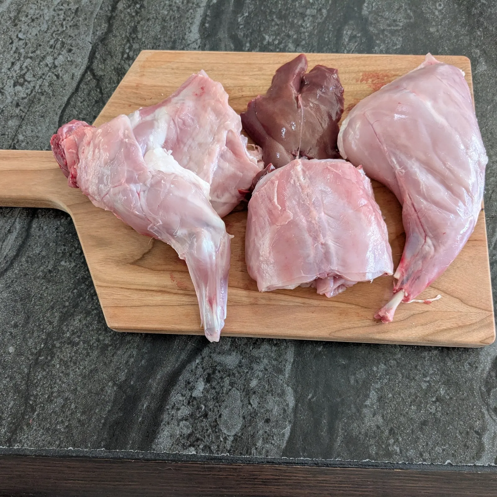 Demi-lapin cru en 3 morceaux avec le foie, sur une planche de bois